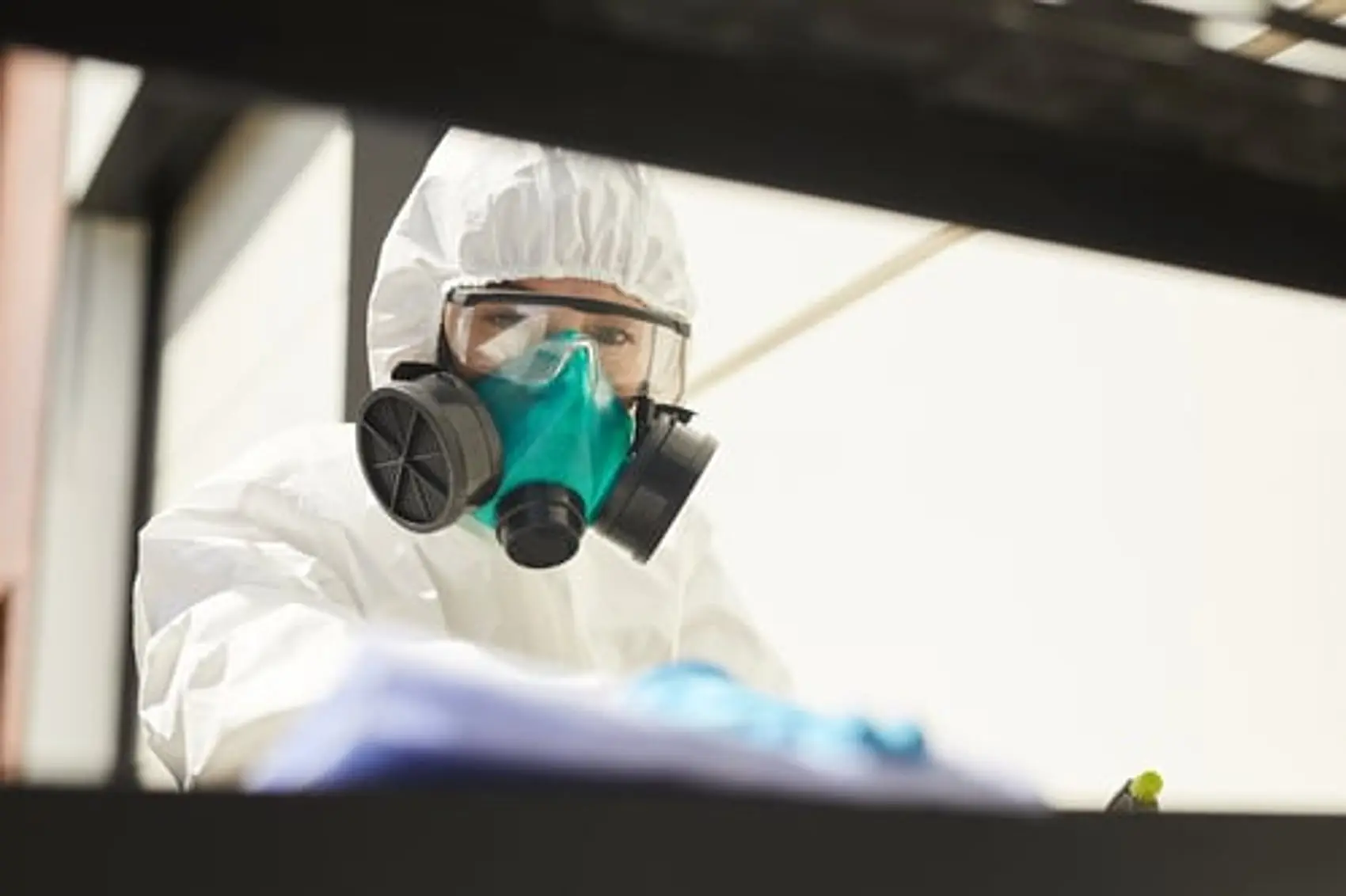 Technician in a white hooded suit and respirator preparing disinfection equipment