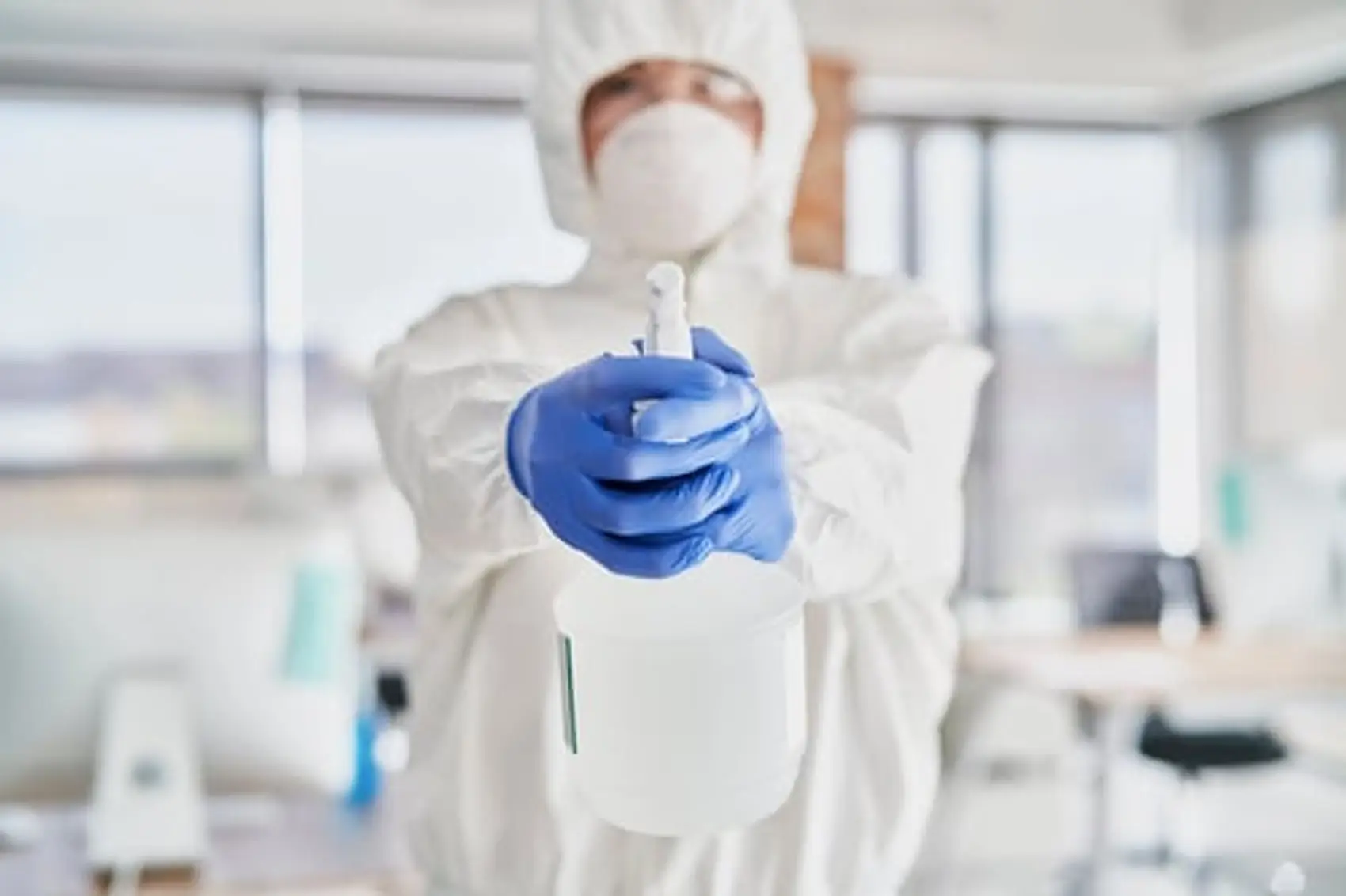 Technician in full PPE holding a disinfectant sprayer